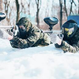 Two paintball players lies on the snow